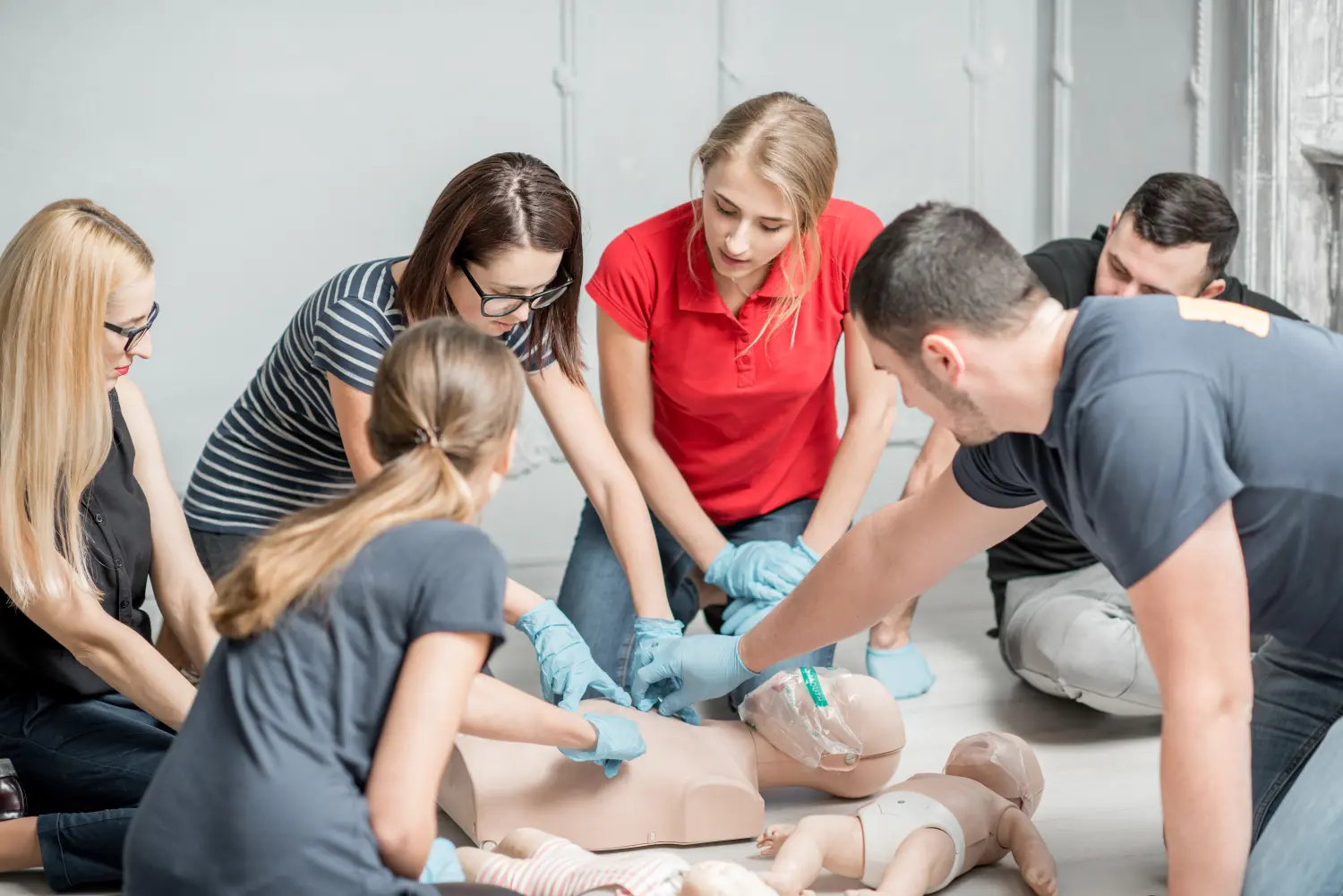 Gruppe von Menschen, die während des Trainings drinnen lernen, wie man mit Dummies Erste-Hilfe-Herzkompressionen durchführt